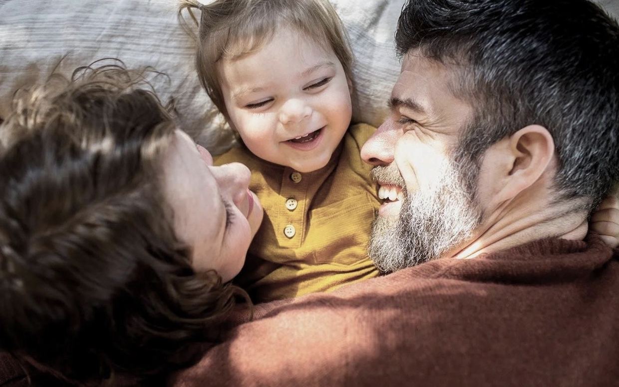 Δύο γονείς ξαπλωμένοι με το μικρό τους παιδί ανάμεσά τους, γελώντας